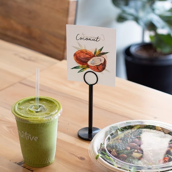 Green smoothie, salad bowl, and a coconut sign on a wooden table at a restaurant.