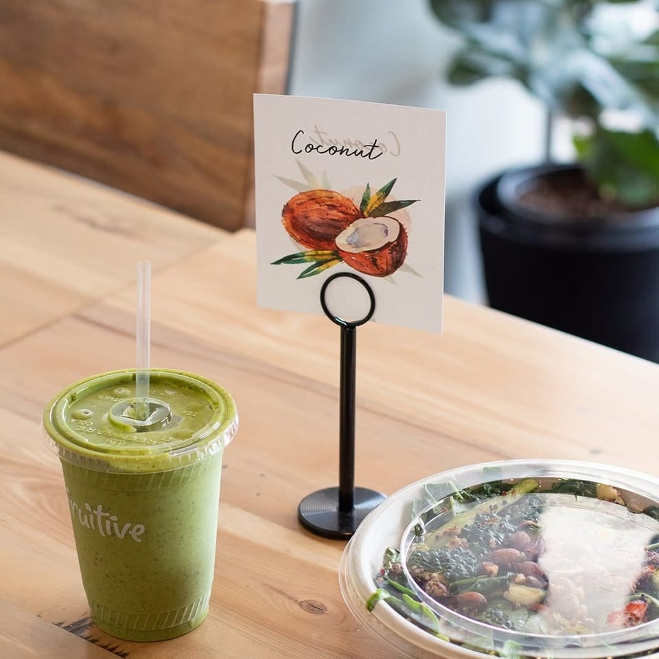 Green smoothie, salad bowl, and a coconut sign on a wooden table at a restaurant.