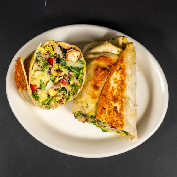 Two grilled wraps, one cut open to show chicken, lettuce, corn, and red peppers, on a white plate.