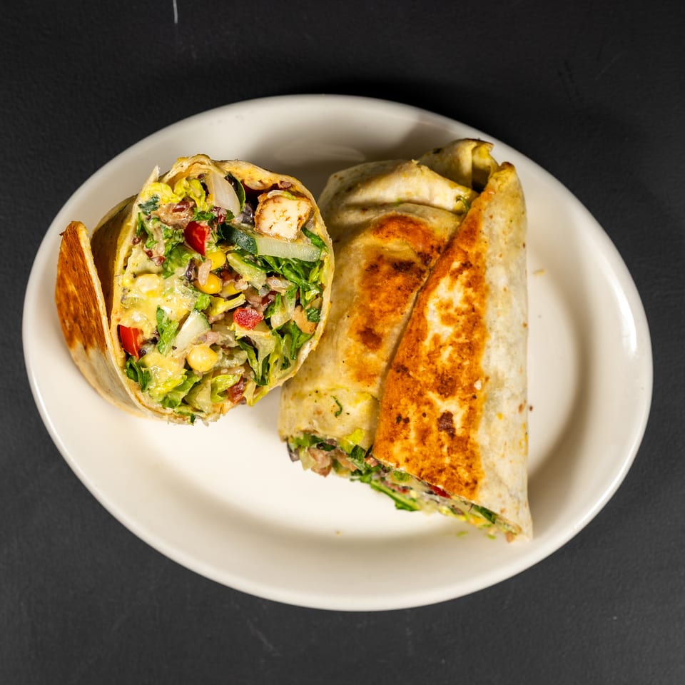 Two grilled wraps, one cut open to show chicken, lettuce, corn, and red peppers, on a white plate.