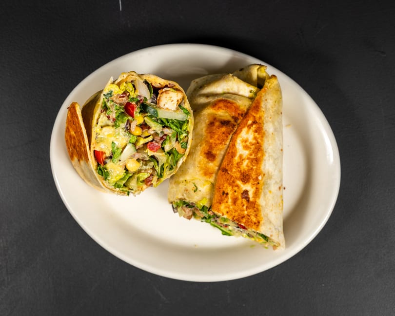 Two grilled wraps, one cut open to show chicken, lettuce, corn, and red peppers, on a white plate.