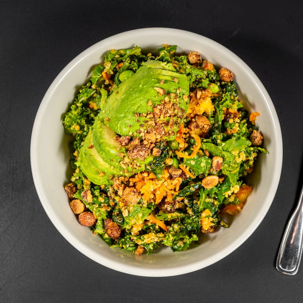 Overhead view of a vibrant kale and quinoa salad topped with avocado slices and nuts.