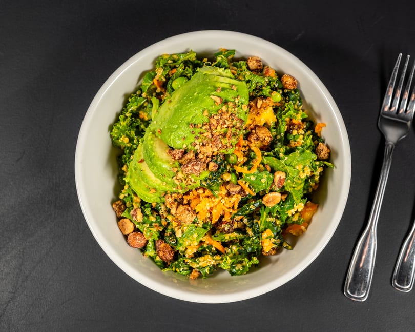 Overhead view of a vibrant kale and quinoa salad topped with avocado slices and nuts.
