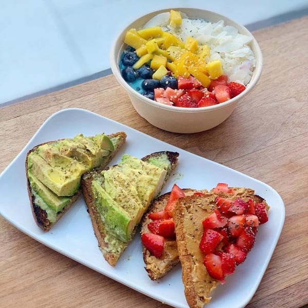 Avocado toast, peanut butter and strawberry toast, and a colorful fruit bowl on a wooden table.