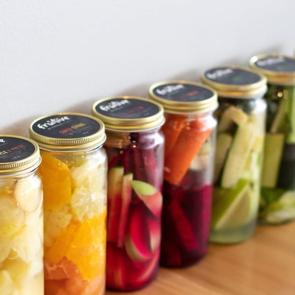 A row of Fruituve produce blends in glass jars, filled with colorful fruits and vegetables.