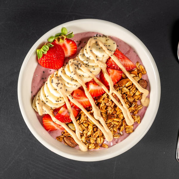 Overhead view of a smoothie bowl with strawberries, bananas, granola, chia seeds, and peanut butter drizzle.