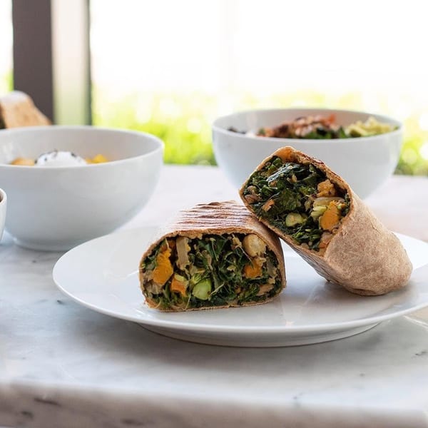 A grilled vegetable wrap, cut in half, on a white plate with bowls of food in the background.
