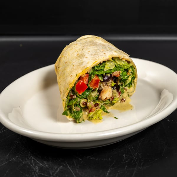 A colorful wrap filled with lettuce, tomatoes, olives, and a creamy dressing on a white plate.