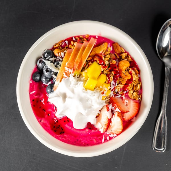 Vibrant pink smoothie bowl topped with blueberries, sliced apples, mango, strawberries, granola, and coconut flakes.