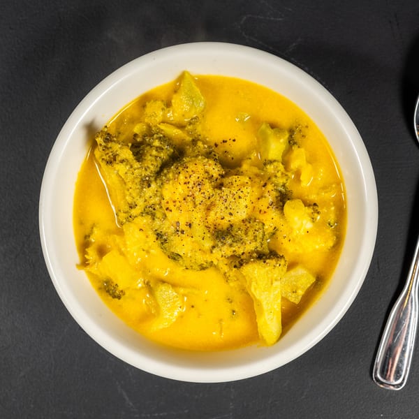 Overhead view of a white bowl filled with yellow curry and broccoli florets, with a spoon beside it.