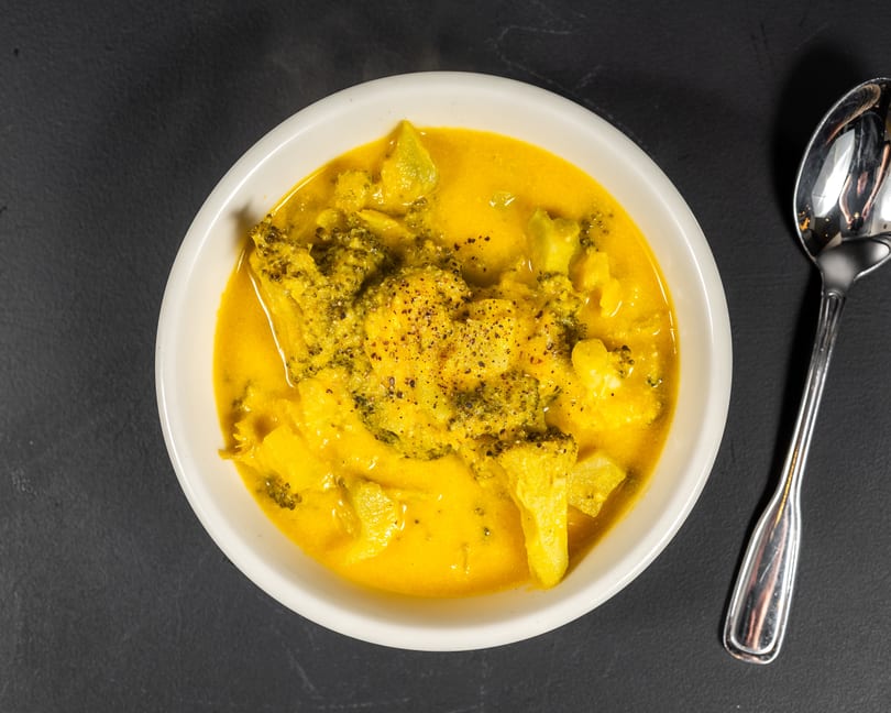 Overhead view of a white bowl filled with yellow curry and broccoli florets, with a spoon beside it.